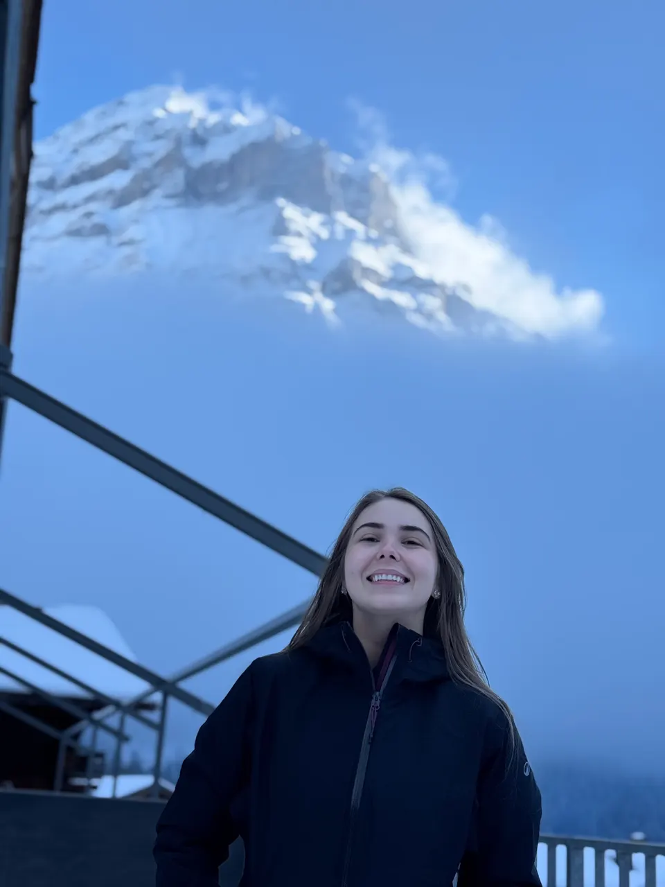 Carolina Perussi sorrindo, de casaco escuro, com uma montanha nevada ao fundo